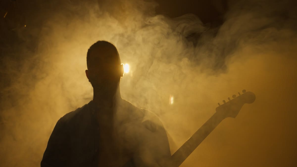 Silhouette de Hicham Berrada à la guitare dans la fumée et la lumière dorée